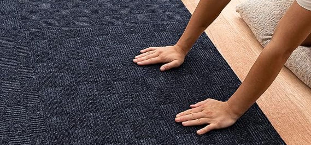 Hands touching dark textured carpet on floor.