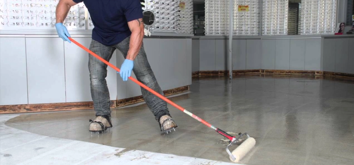 Person applying floor coating with roller tool.