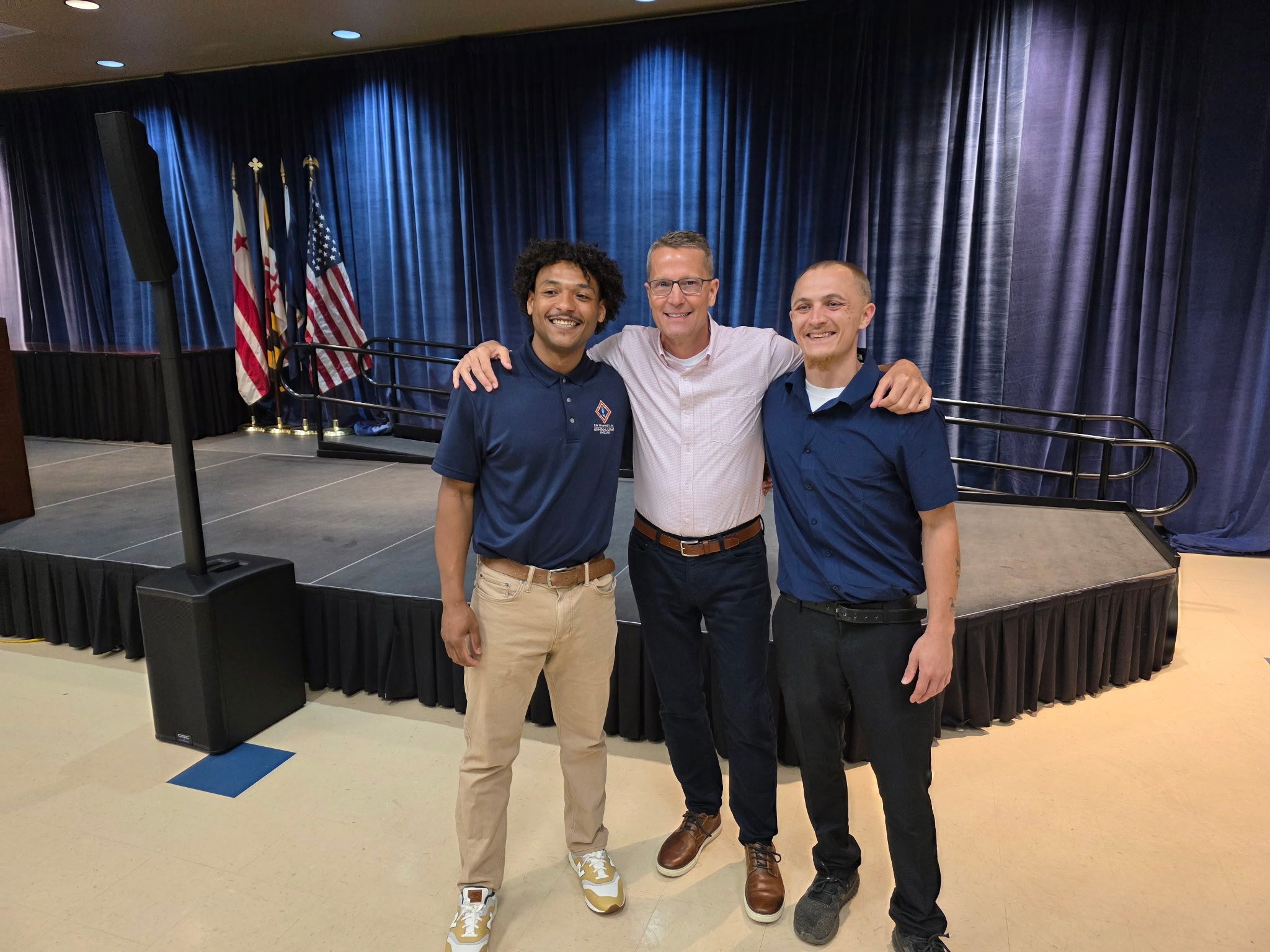 Three men smiling in front of stage.